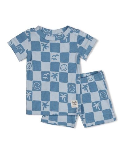 Baby zit op de bank met een verwonderde blik in blauwe shortama
